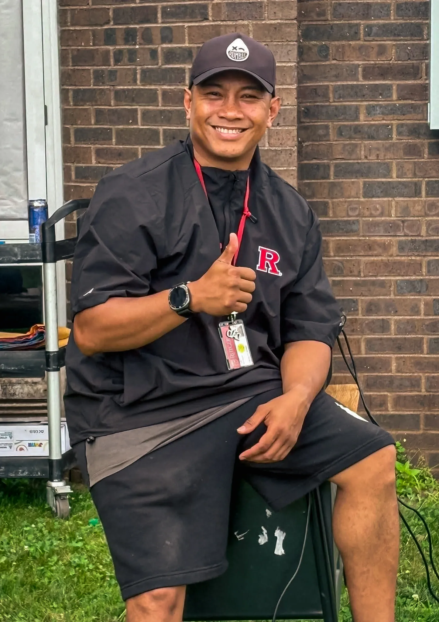 Carlo seated outdoors, smiling and giving a thumbs-up.