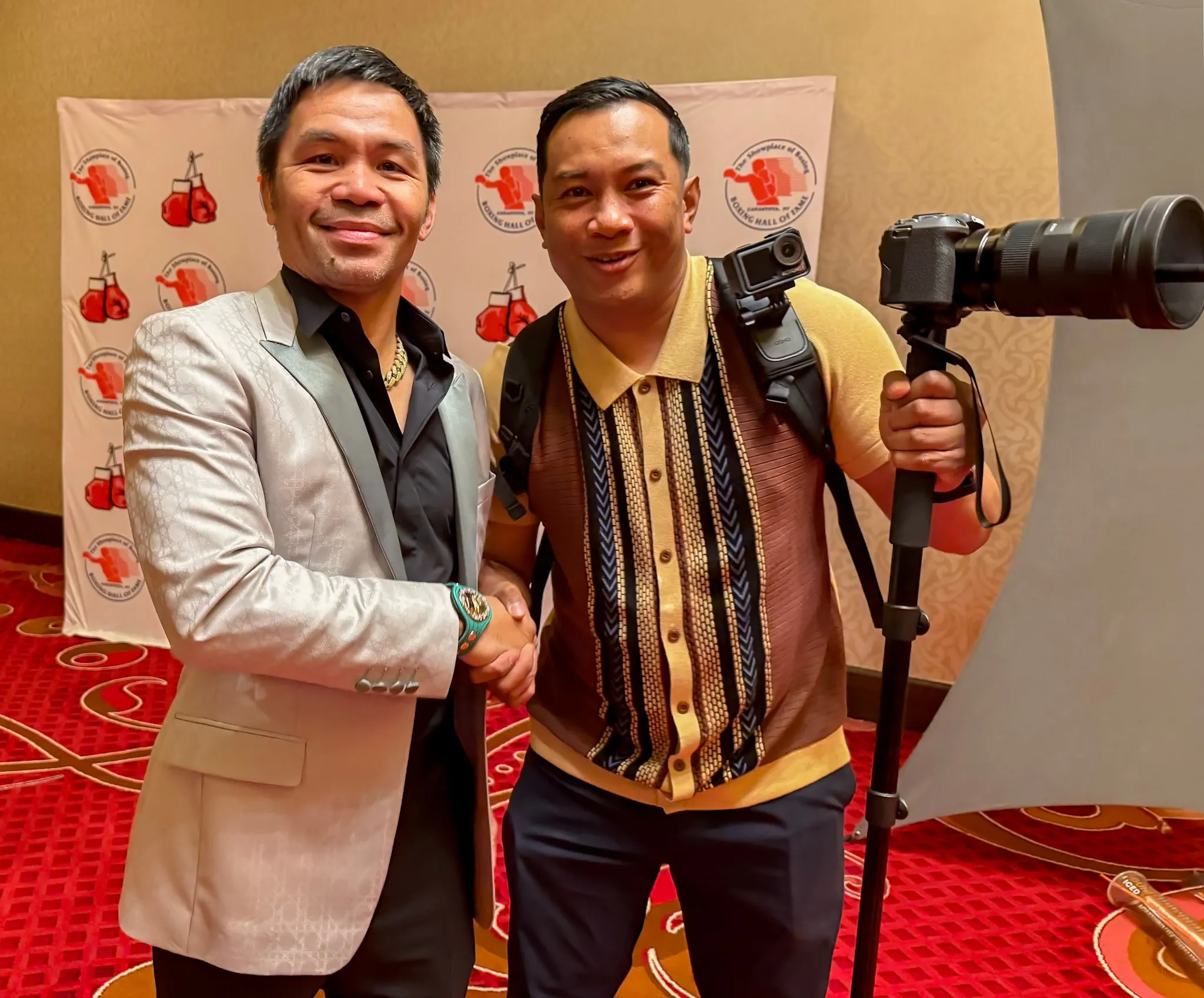 Two men at a boxing event, one holding a camera rig